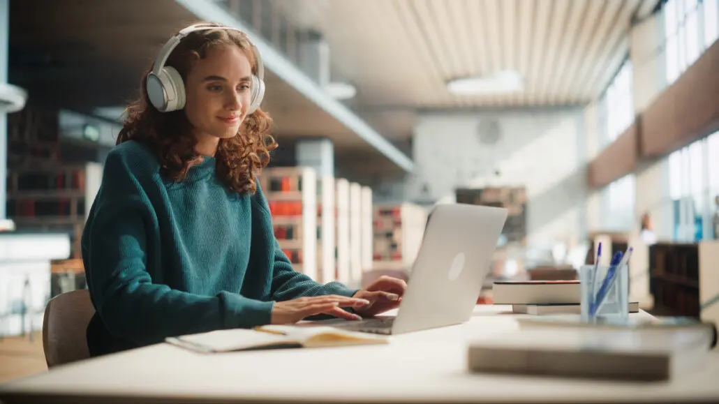 Female student in a library, working on a laptop