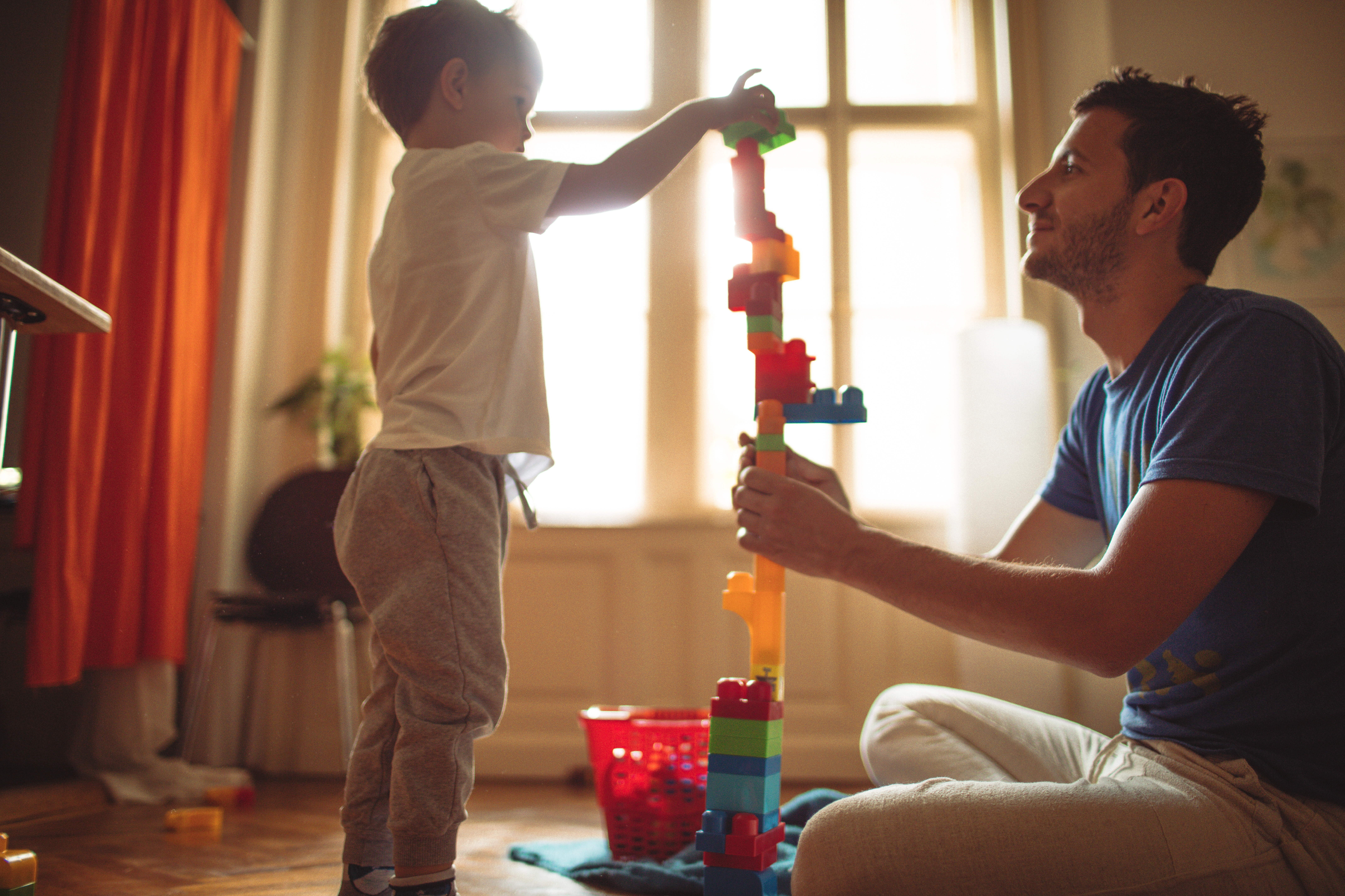 Man and young child play with blocks on floor.
