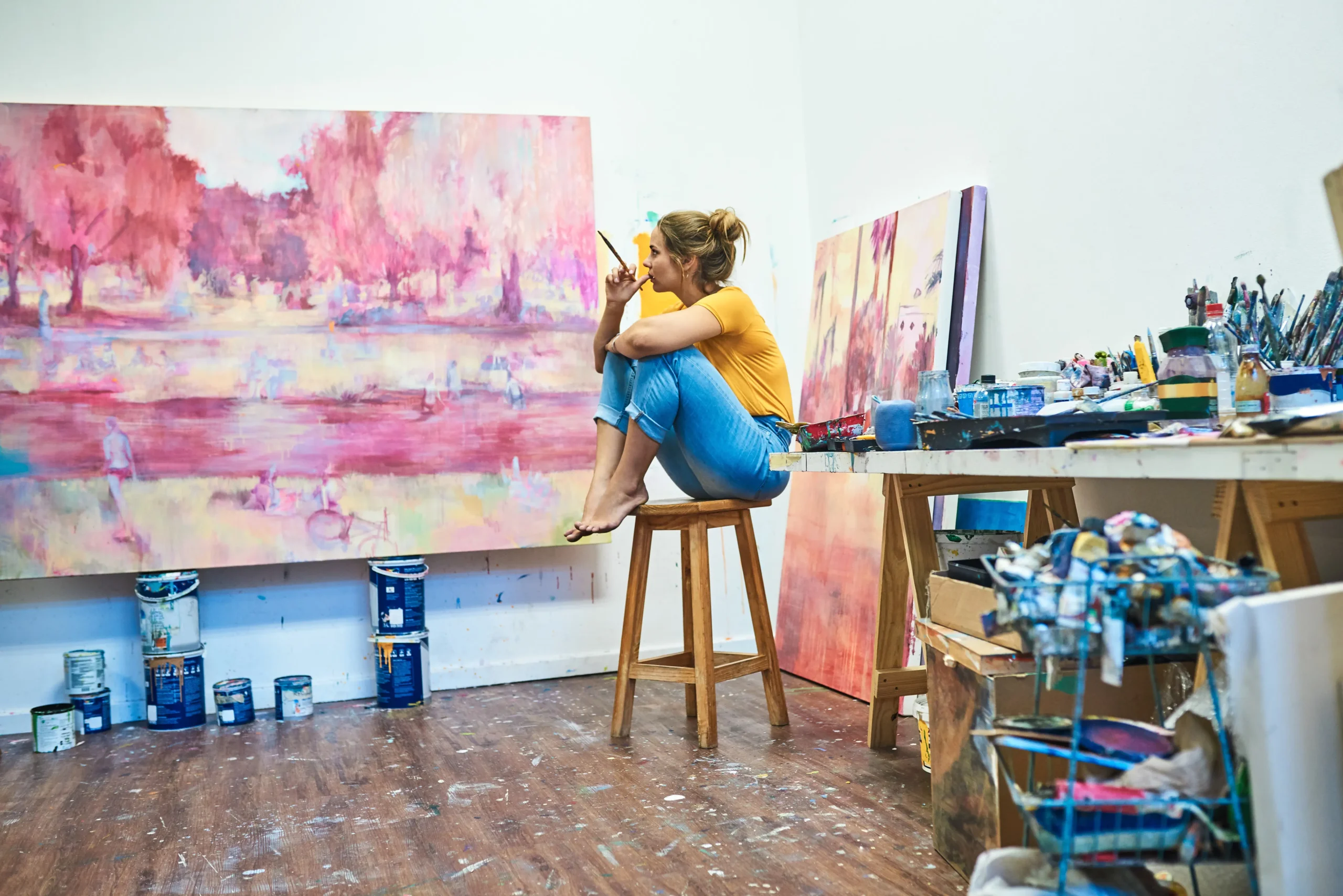 Female painter sitting on stool surrounded by paintings