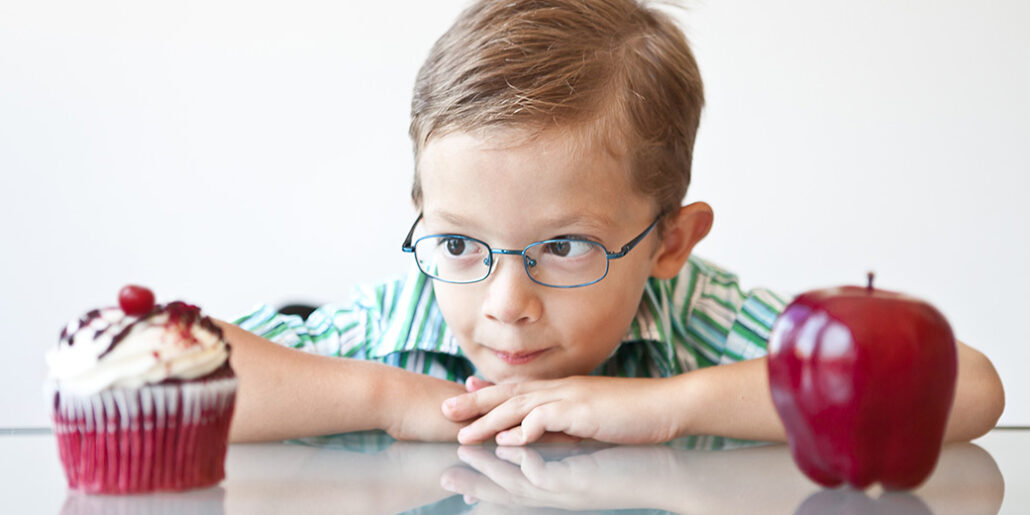 A young boy deciding between a cupcake and an apple.