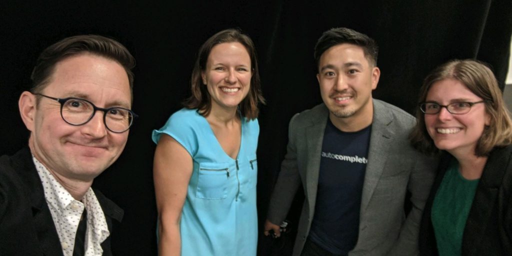 Two men and two women in business casual clothes pose for a selfie photo.