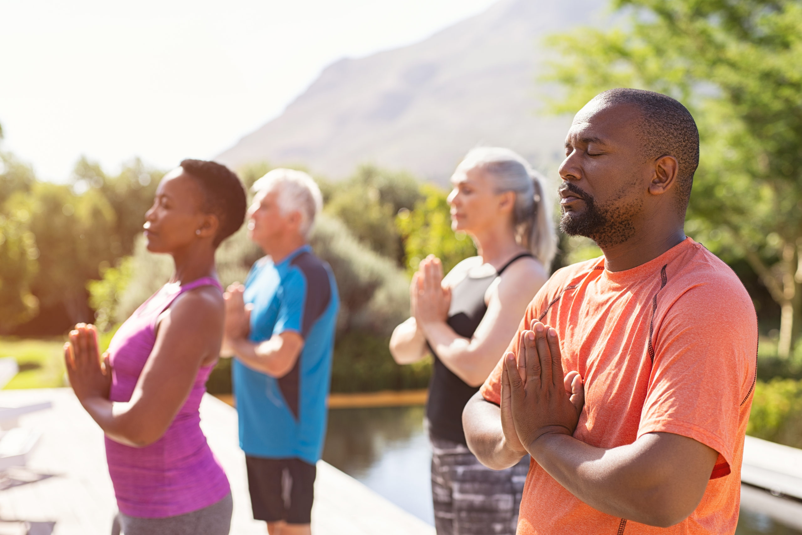 Large group of people meditating in a park outside.