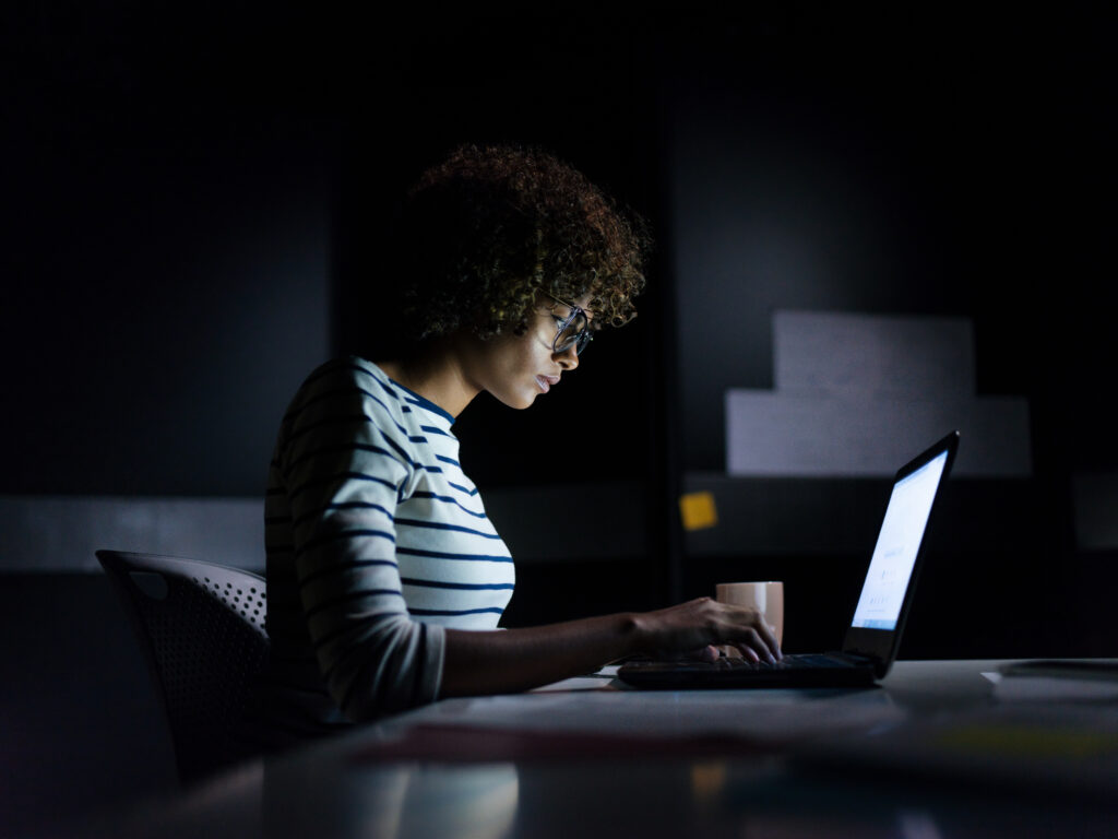 Young Black woman looking at computer screen in a darkened room.
