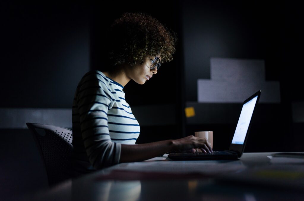 Young Black woman in front of computer screen in darkened room