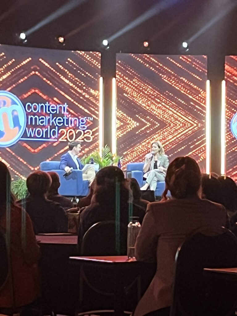 An audience view of two presenters on the stage at CMWorld 2023.