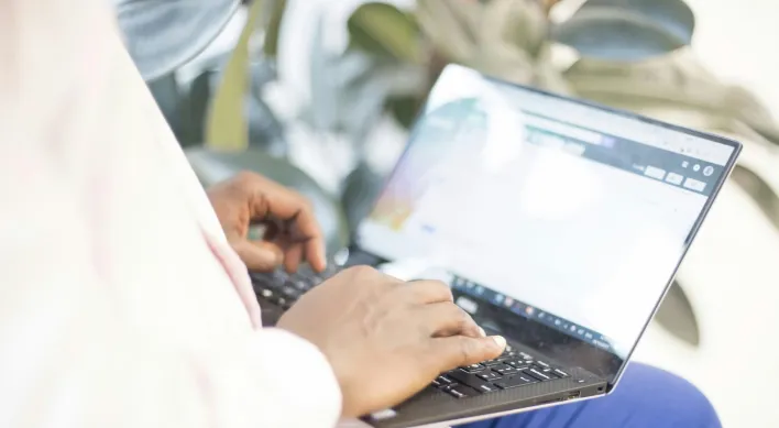 Person sitting on bench with laptop in their lap.