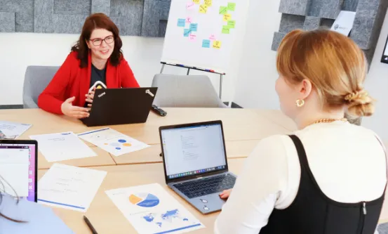 Office staff sitting at a conference table using their laptops while in discussion.